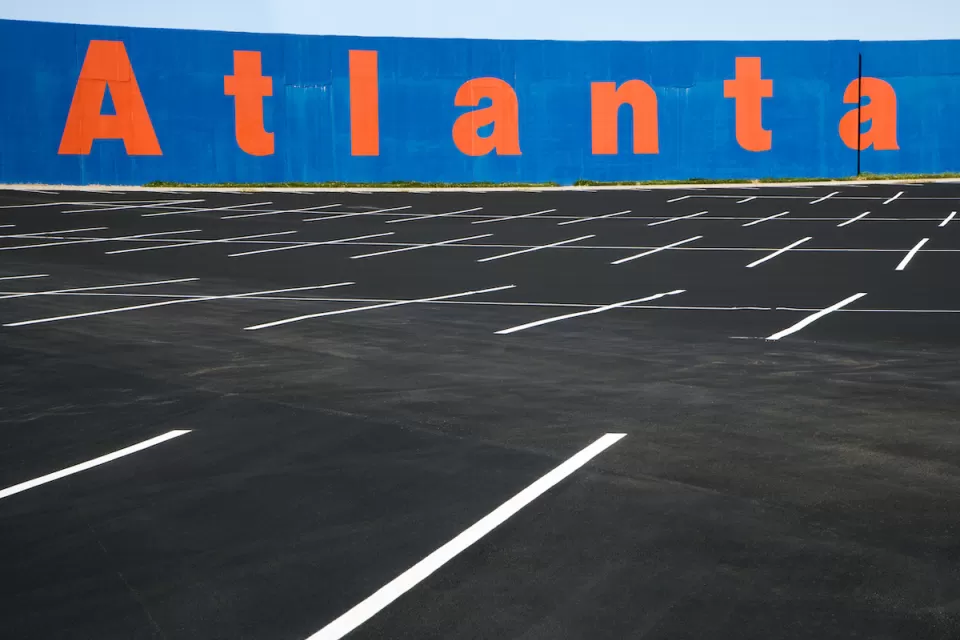Empty asphalt parking lot with blue wall in background with Atlanta painted in orange letters.